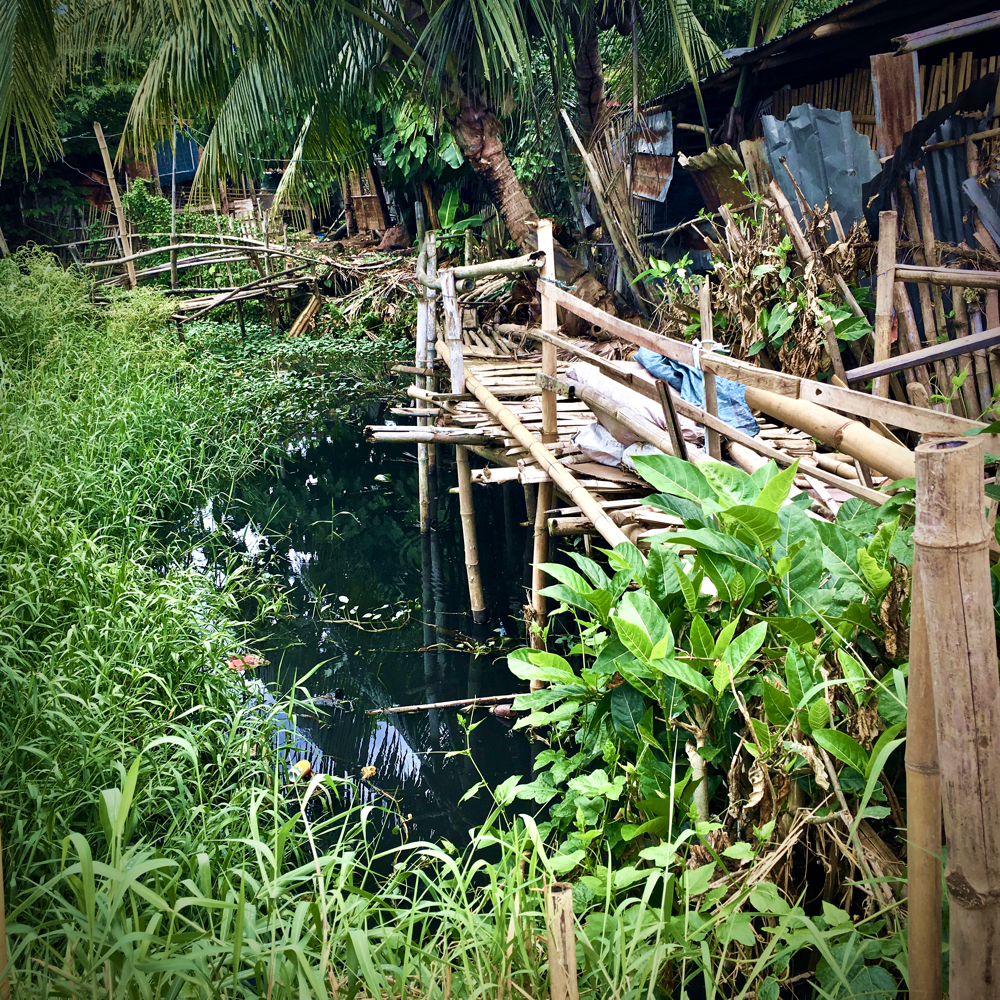 a tangle of makeshift bamboo walkways sit next to a massive shopping centre (Balasan) Philippines by Melinda J. Irvine