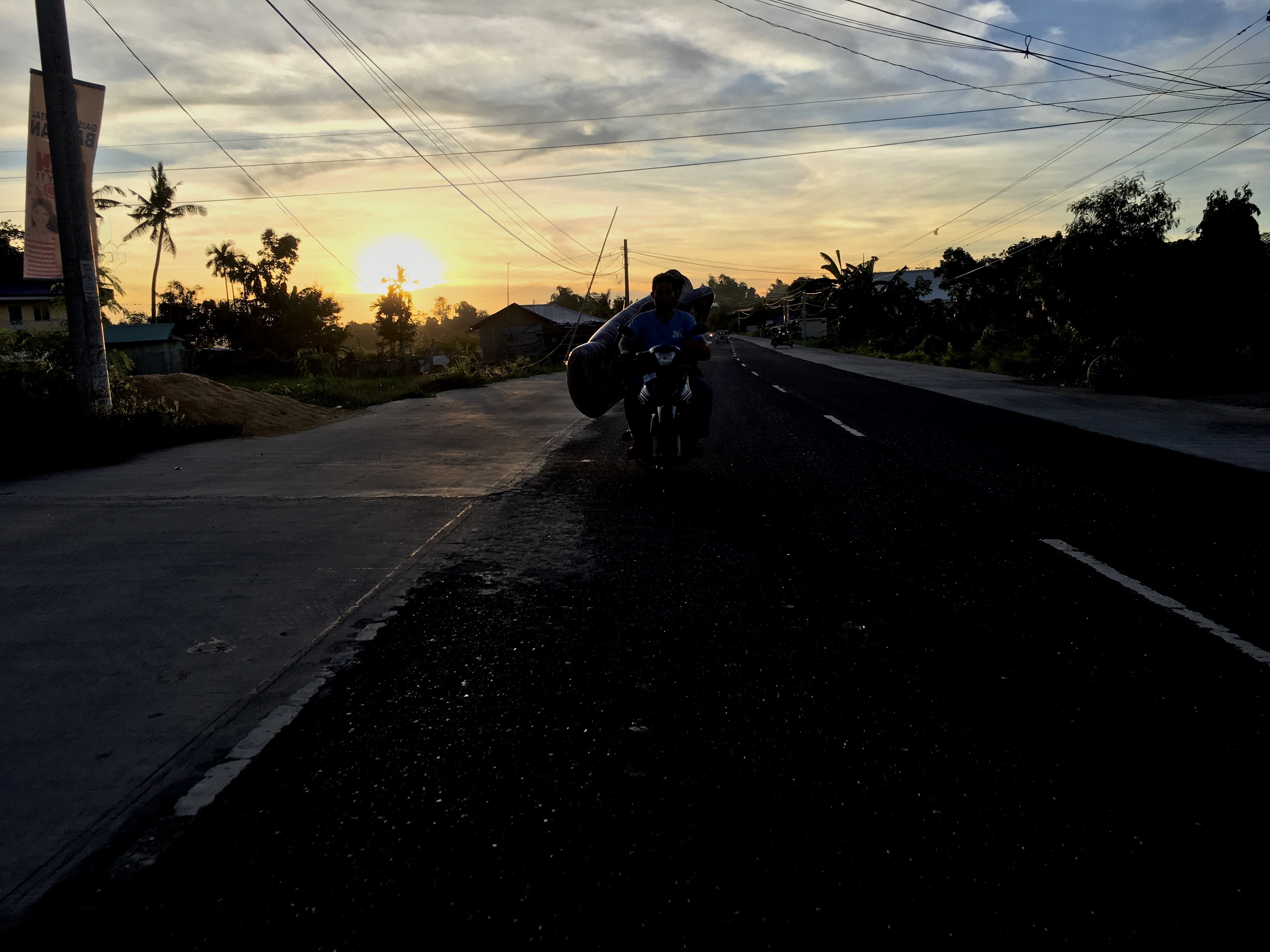 overloaded motorbike with no headlights driving at sunset by Melinda J. Irvine