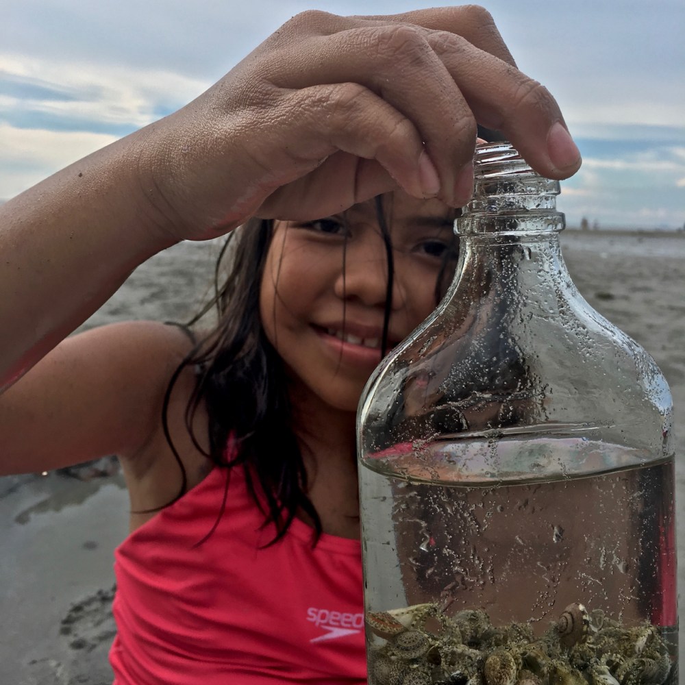 Filipino girl at the beach with a bottle of shells
