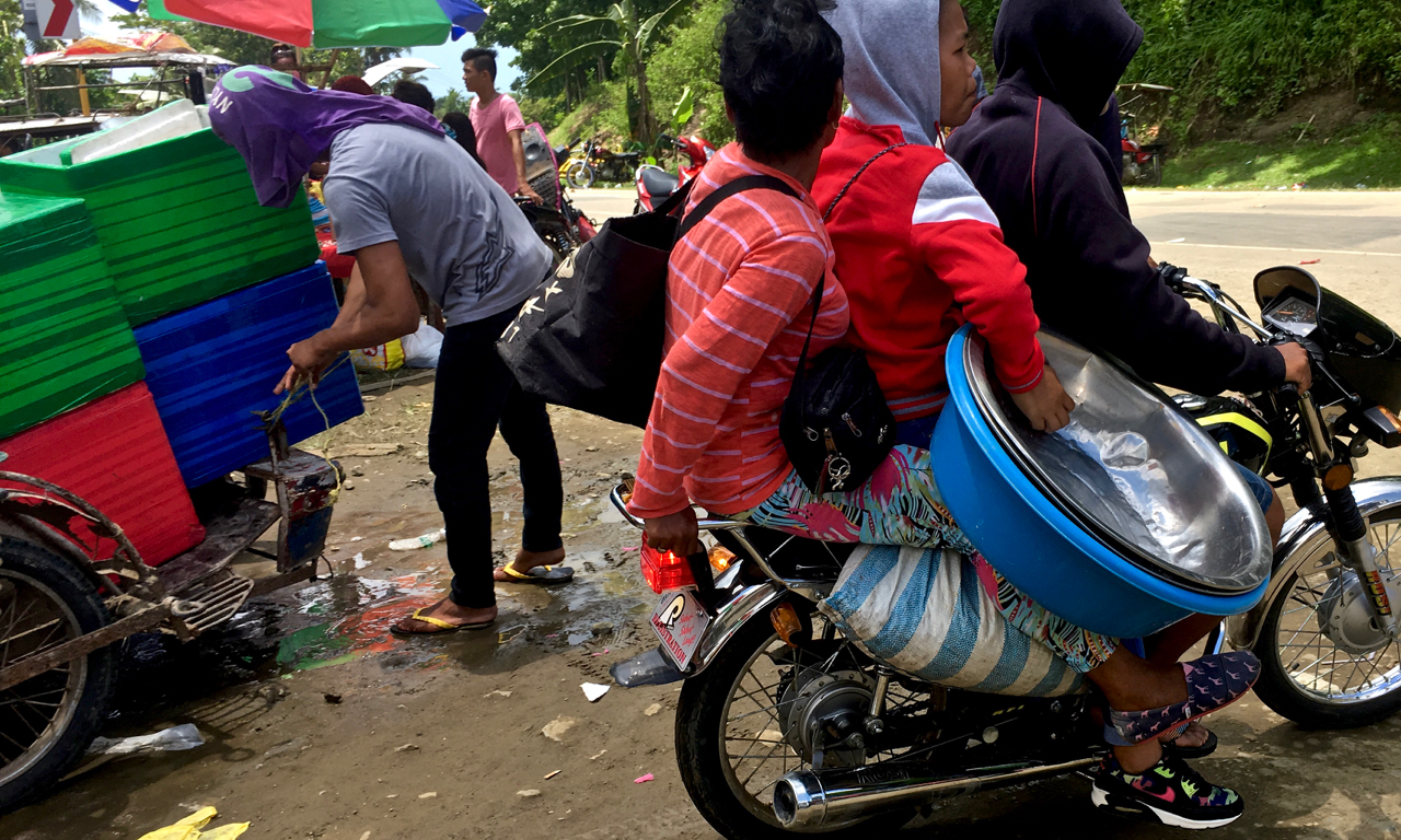 overloaded motorcycle trasnports a stall holder home from a religous festival in rural Philippines